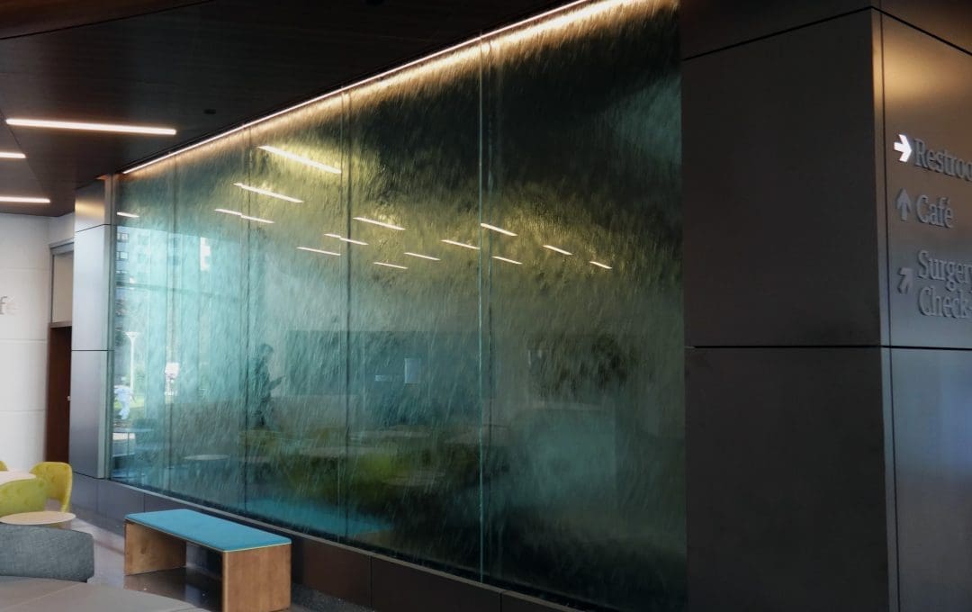 Blu-Guard sealed water feature located in a hospital lobby. This water wall has blue mirror glass and white LED lighting from above.