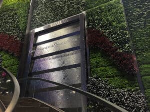This water feature is a stainless steel ship lapped vertical feature surrounded by a green wall creating a biophilic design. It also features a signage logo floating in front. 